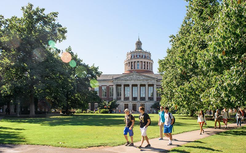 Photo of students with backpacks walking across Eastman Quad in front of Rush Rhees Library on River Campus