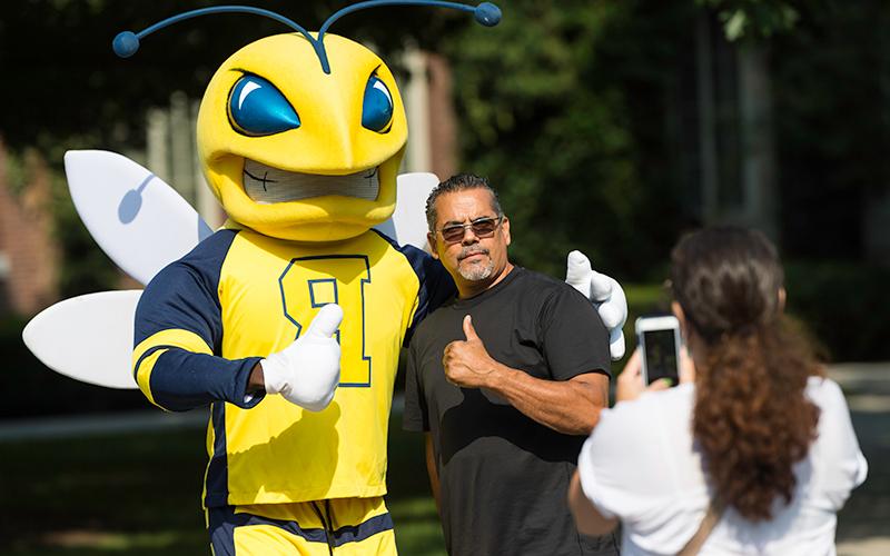 Photo of a woman taking a photo of a man posing with University of Rochester mascot, Rocky