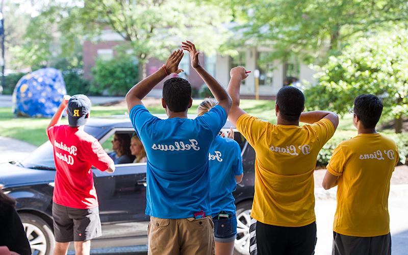 Photo of several student volunteers cheering as a car pulls up to a residence hall during new student move-in