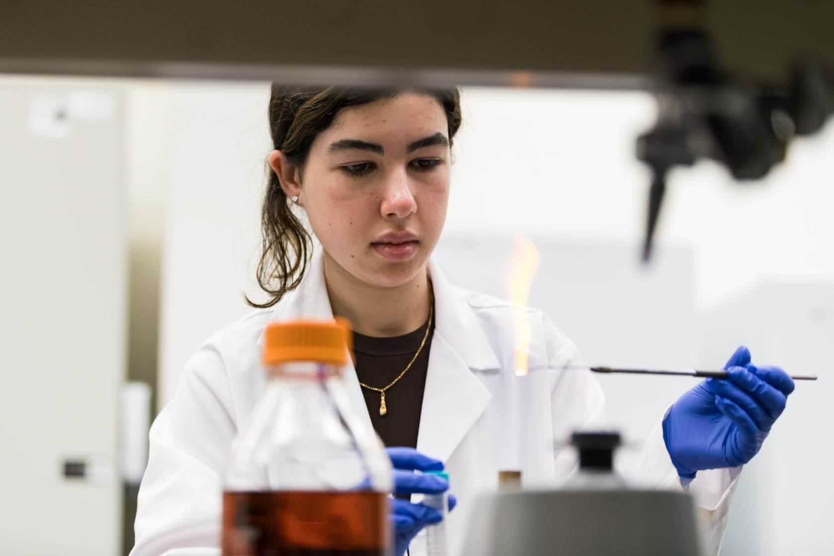 Ines Drissi Qeytoni '26 prepares bacteria overnight cultures; sterilizes an inoculation loop under flame. // Students work on experiments for the 2023 iGEM competition in the lab of Associate Professor of Biology Anne S. Meyer in Hutchison Hall August 17, 2023. The International Genetically Engineered Machine (iGEM) competition is a worldwide synthetic biology competition intended to push the boundaries of synthetic biology by tackling everyday issues facing the world. // photo by J. Adam Fenster / University of Rochester